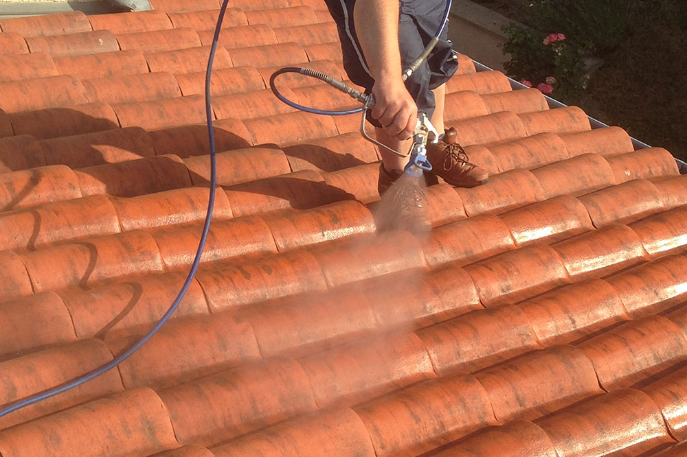Couvreur en train de pulvériser un traitement hydrofuge sur une toiture en tuiles