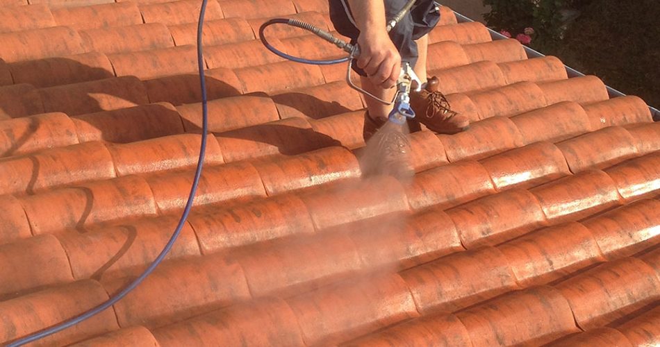 Couvreur en train de pulvériser un traitement hydrofuge sur une toiture en tuiles